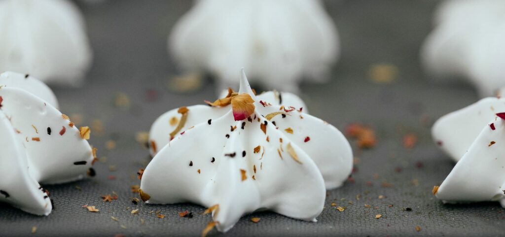 Meringues blanches avec des épices colorées sur une plaque de cuisson, mettant en valeur le détail et la texture.