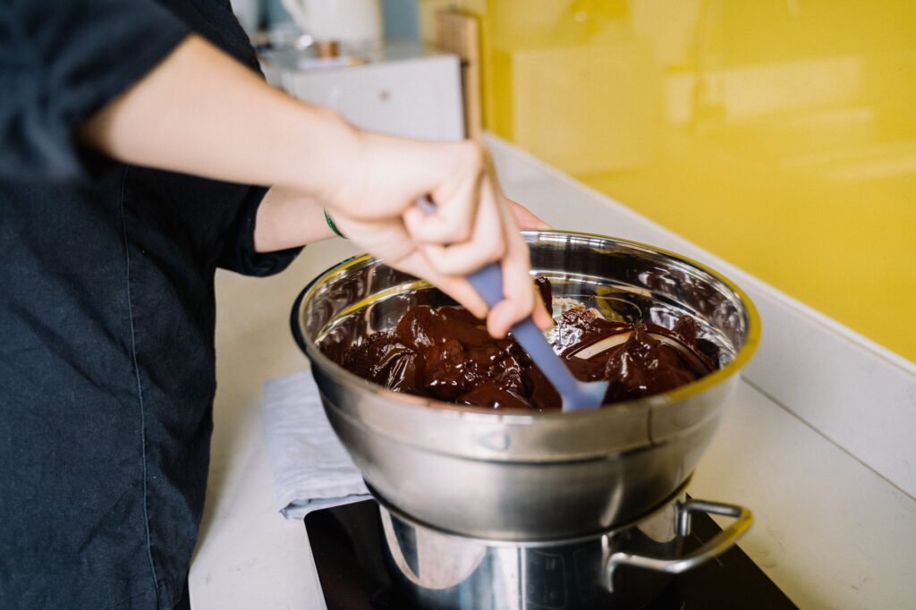 Une personne mélange du chocolat fondu riche dans un bol en acier inoxydable pour la préparation de desserts.
