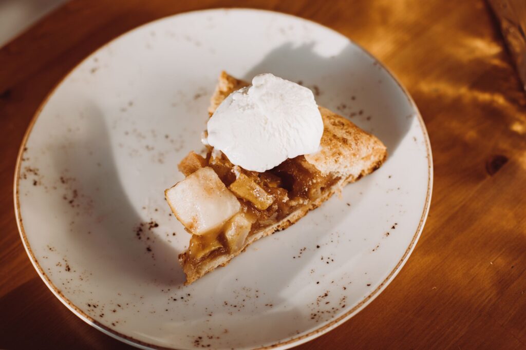 Une délicieuse tranche de tarte aux pommes, surmontée de crème fouettée, sur une assiette en céramique rustique.