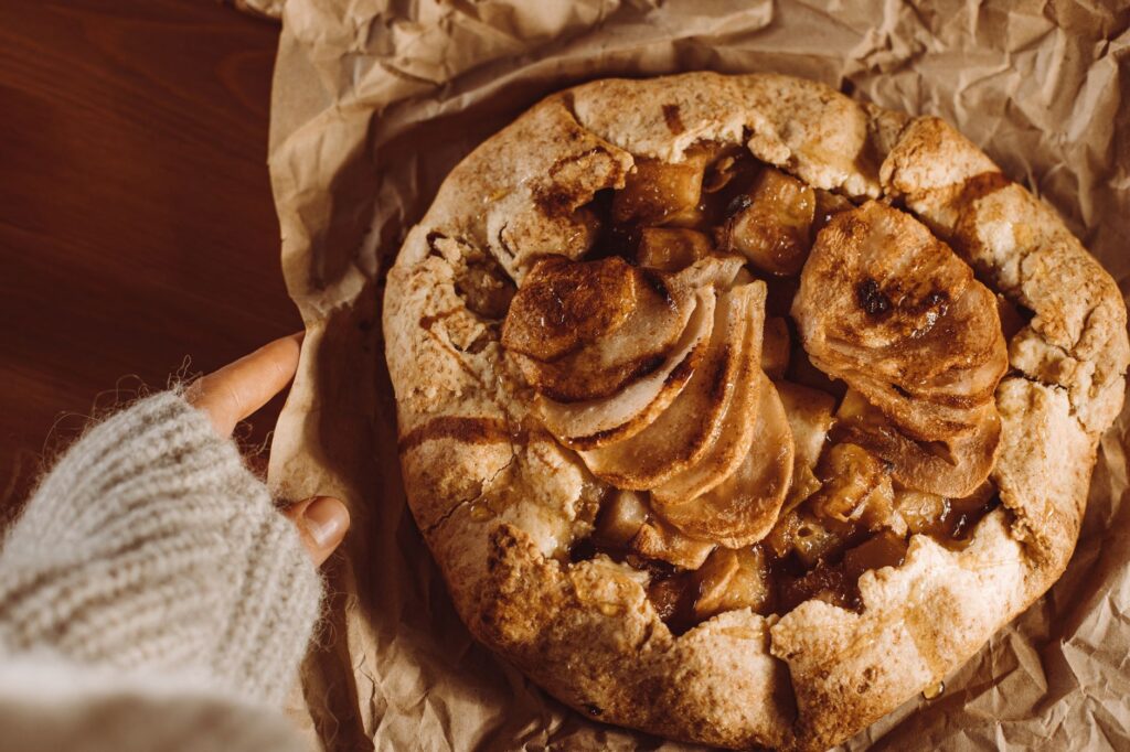 Une vue du dessus d'une galette de pommes maison sur du papier brun avec un pull douillet en arrière-plan.