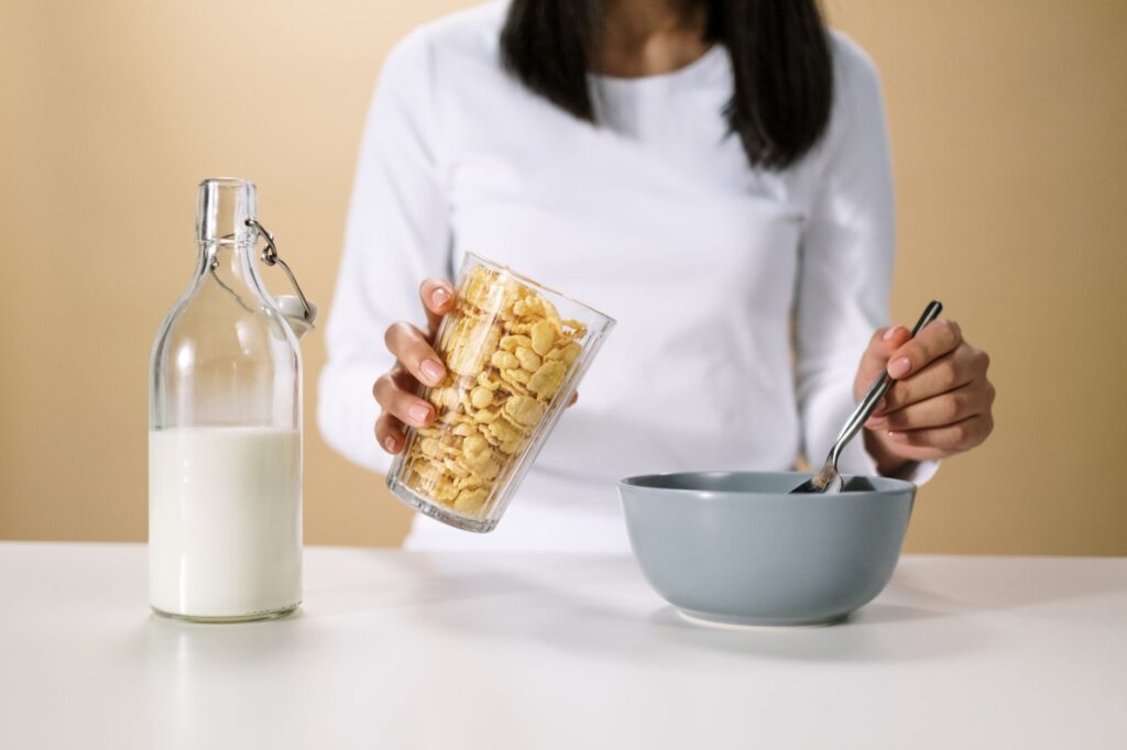 Personne versant des céréales dans un bol avec une bouteille de lait à proximité, prête pour le petit déjeuner.