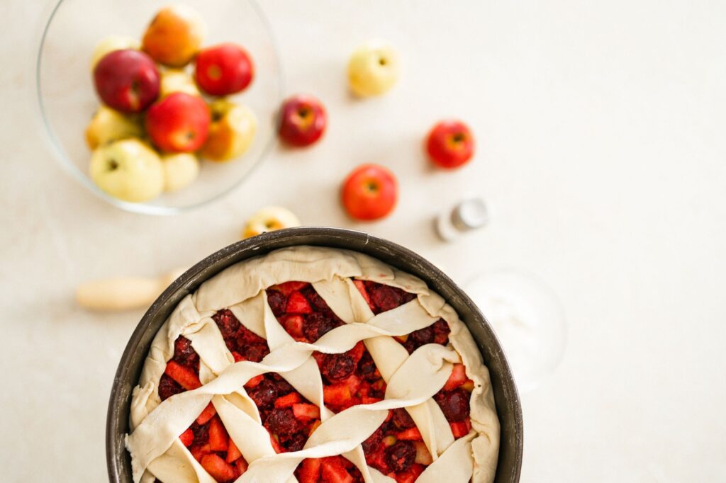 Tarte aux pommes et cerises fraîches prête à cuire, accompagnée de pommes colorées.