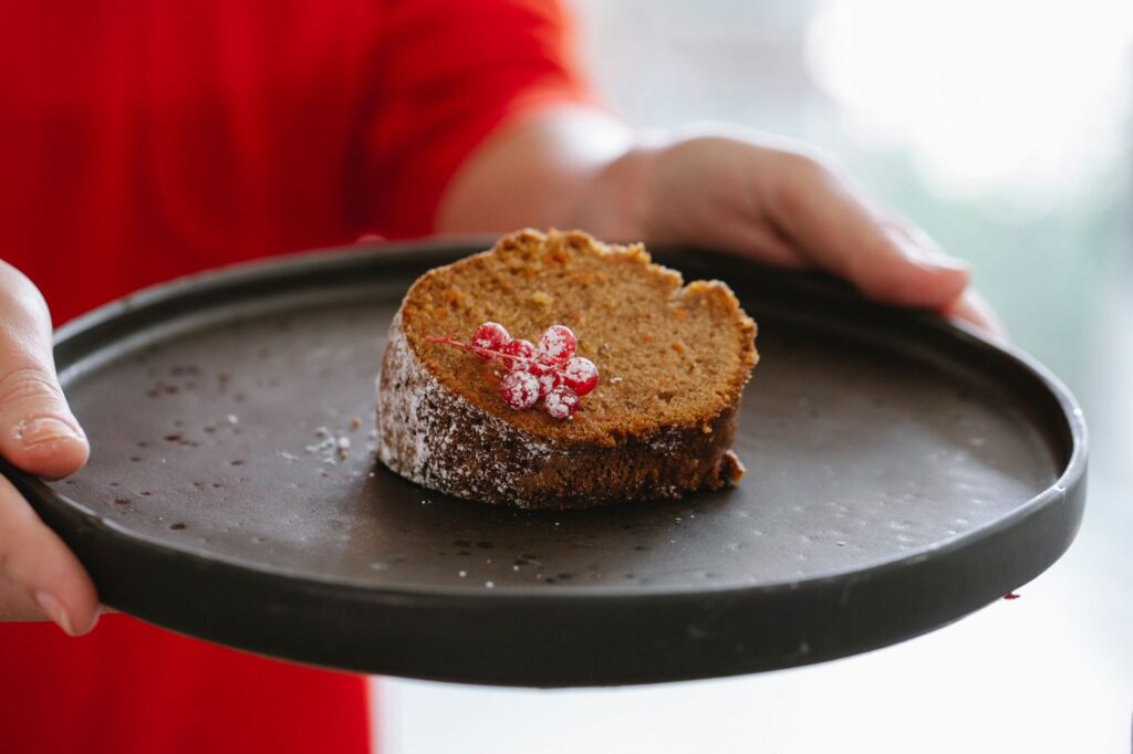 Une part de gâteau tentante avec des groseilles rouges sur une assiette noire, parfaite pour les amateurs de desserts.