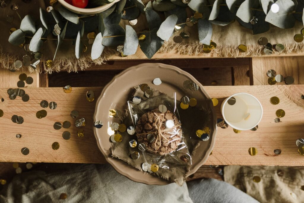 Une table rustique avec un cookie emballé et des confettis, évoquant une atmosphère festive.