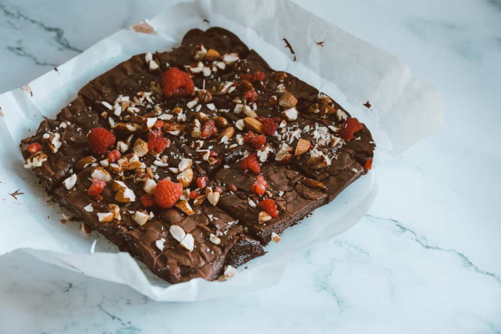Brownie au chocolat fraîchement cuit, garni d'amandes et de framboises sur du papier sulfurisé.