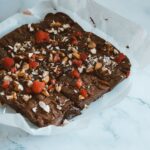 Brownie au chocolat fraîchement cuit, garni d'amandes et de framboises sur du papier sulfurisé.
