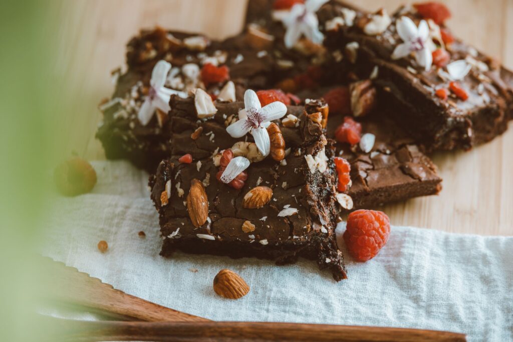 Gros plan sur des brownies au chocolat ornés d'amandes, de framboises et de fleurs blanches sur une planche en bois.