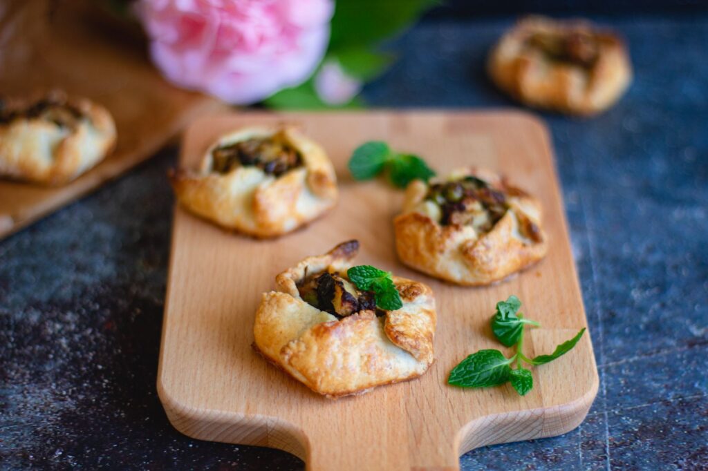 Mini pâtisseries cuites servies avec des feuilles de menthe sur une planche en bois, parfaites pour des présentations culinaires.