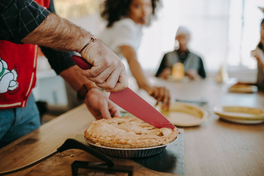 Une personne découpe une tarte maison lors d'un rassemblement familial dans un cadre intérieur confortable.
