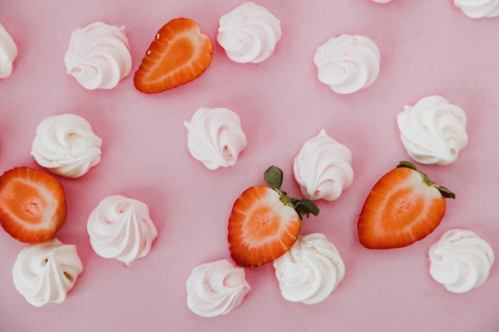 Gros plan de fraises tranchées et de tourbillons de meringue sur un fond rose.