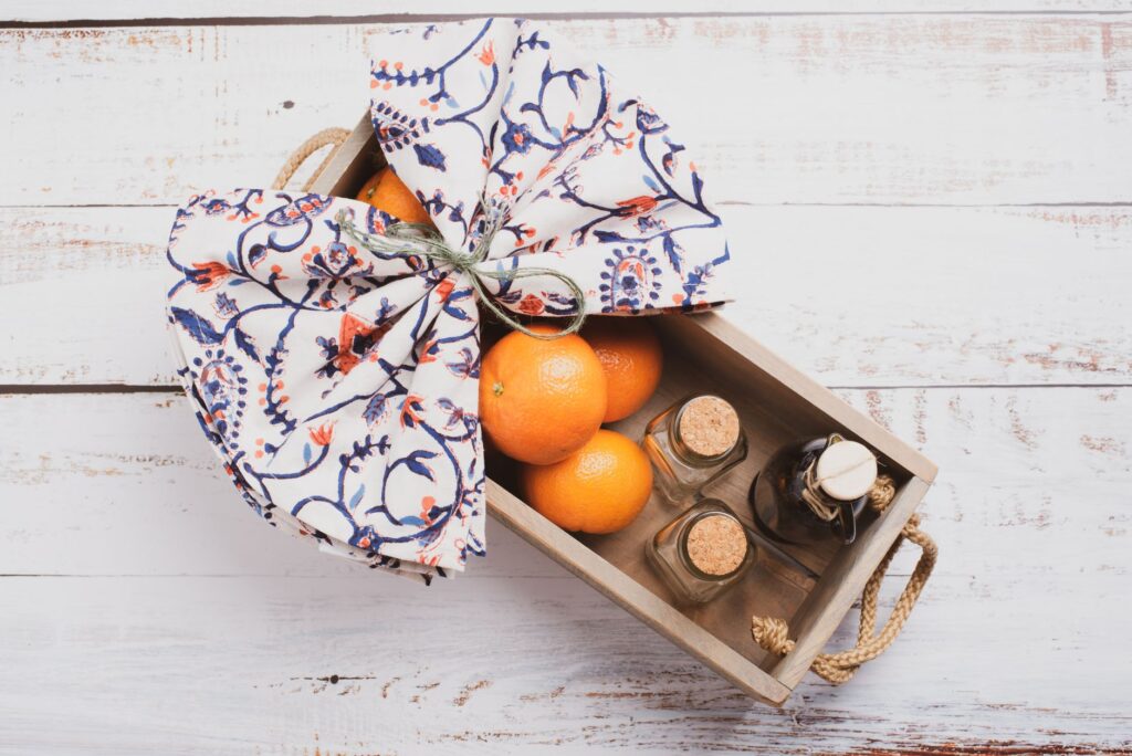 Une boîte en bois remplie d'oranges et de bocaux en verre sur un fond blanc rustique, recouverte d'un tissu décoratif.