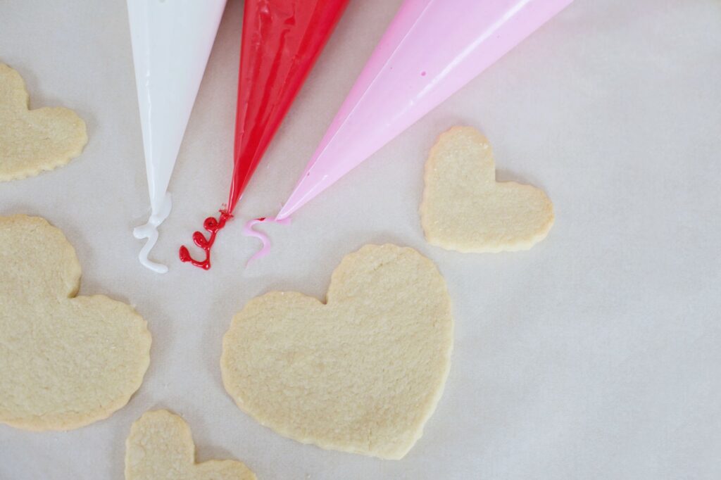 Biscuits en forme de cœur prêts à être décorés avec des poches à douille colorées.