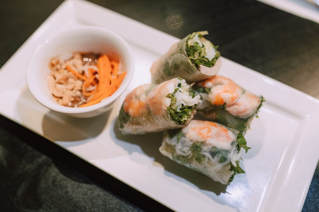 Gros plan sur des rouleaux de printemps vietnamiens avec des crevettes et une sauce de trempage sur une assiette blanche.