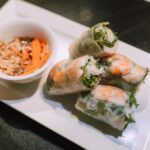 Gros plan sur des rouleaux de printemps vietnamiens avec des crevettes et une sauce de trempage sur une assiette blanche.