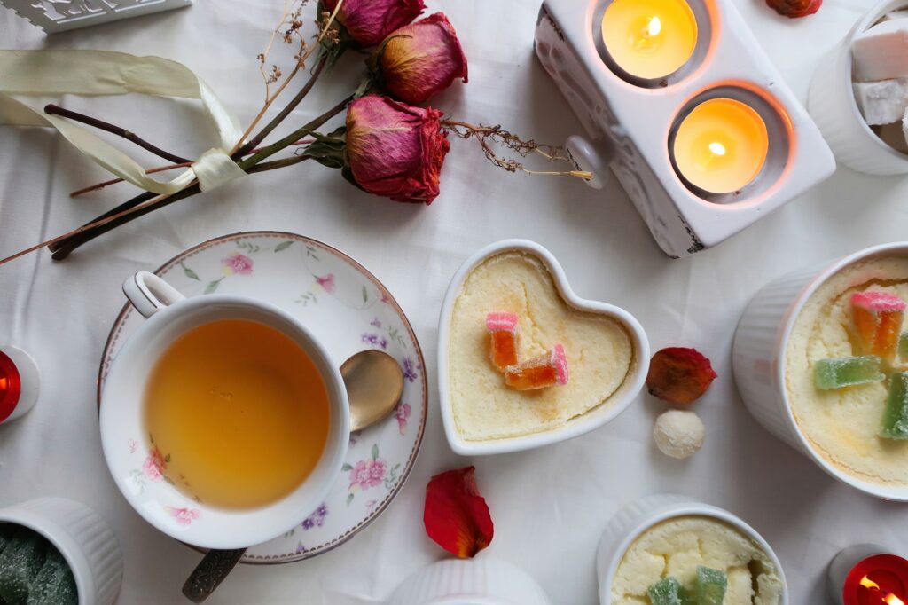 Une ambiance chaleureuse et confortable avec du thé, des desserts en forme de cœur, des bougies et des roses séchées sur un tissu blanc.