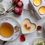 Une ambiance chaleureuse et confortable avec du thé, des desserts en forme de cœur, des bougies et des roses séchées sur un tissu blanc.