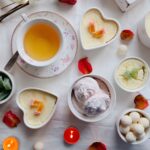 Élégante composition à plat de thé et de desserts avec des bougies et des pétales pour une atmosphère cozy.