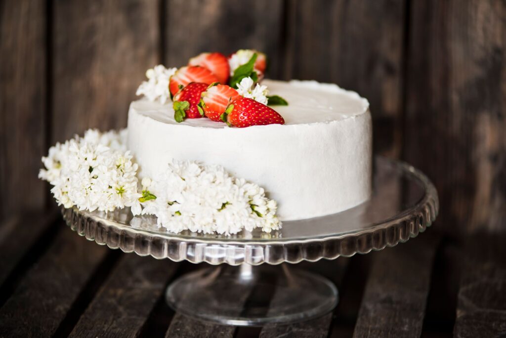 Un gâteau magnifiquement décoré avec des fraises et des fleurs sur un support en verre.