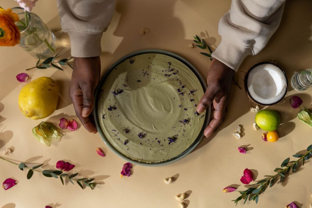 Vue de dessus d'un gâteau vegan au matcha avec des décorations florales et fruitées vibrantes, tenu par des mains.