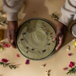 Vue de dessus d'un gâteau vegan au matcha avec des décorations florales et fruitées vibrantes, tenu par des mains.