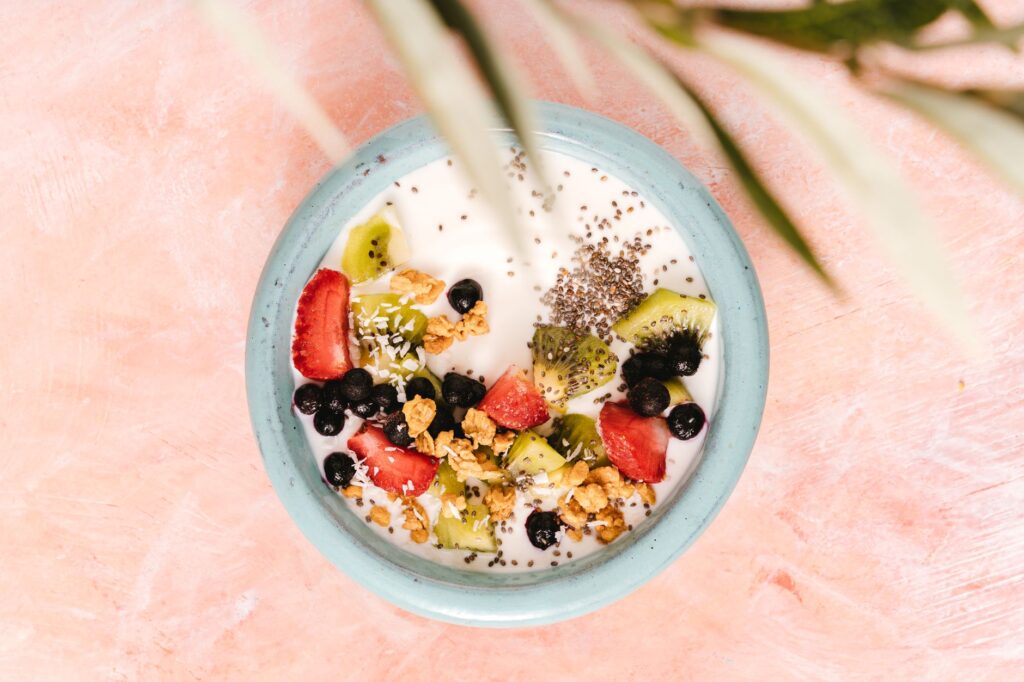 Vue de dessus d'un bol de petit-déjeuner sain avec du yaourt, des fruits, et des graines sur un fond rose.