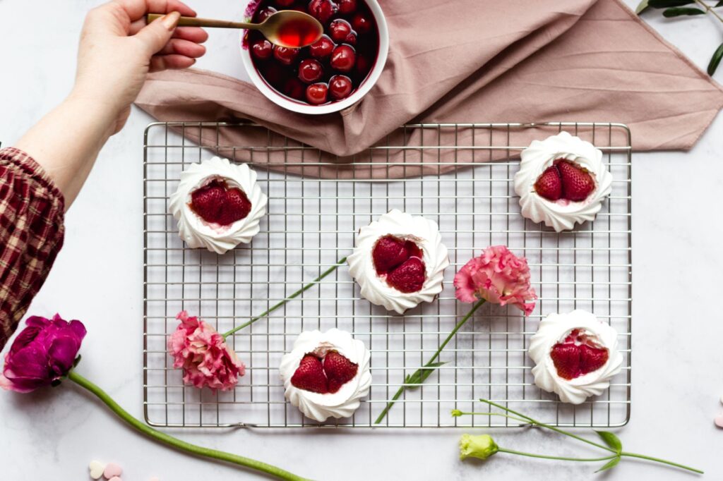Vue de dessus de desserts à la meringue de fraise avec des cerises fraîches et des fleurs, parfaits pour le stylisme culinaire et le contenu de blog.