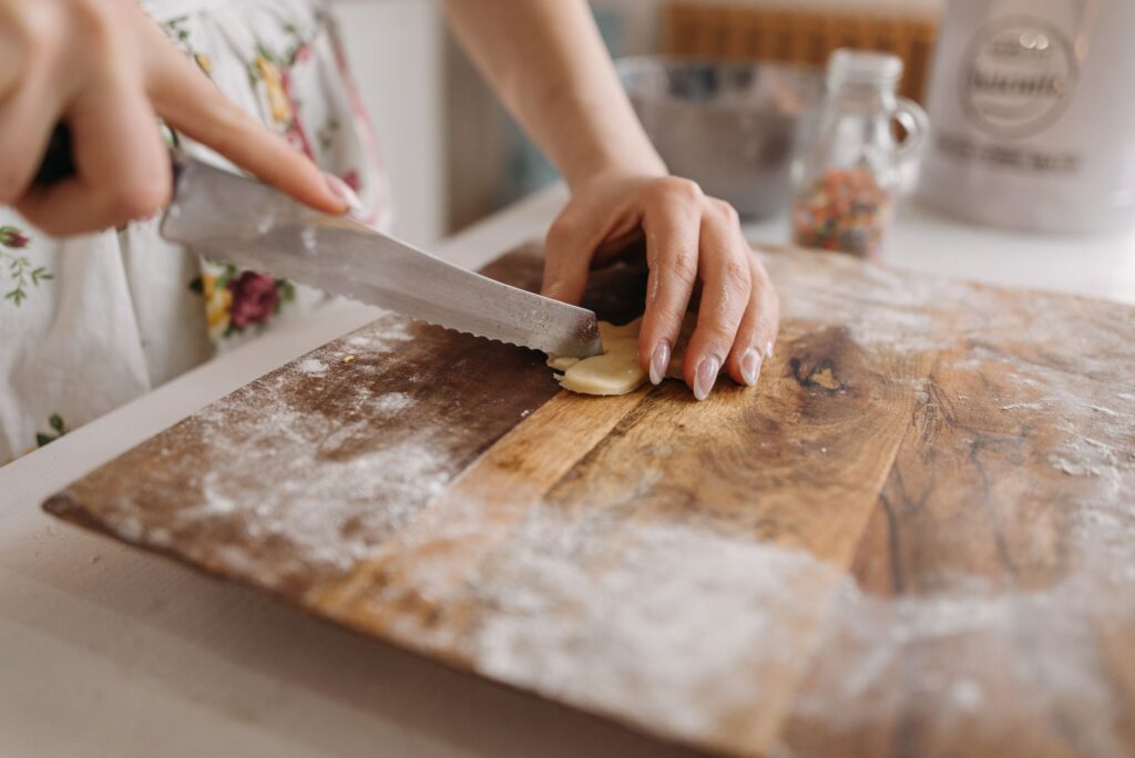 Gros plan sur des mains tranchant habilement de la pâte à cookies sur une planche en bois fariné dans la cuisine.