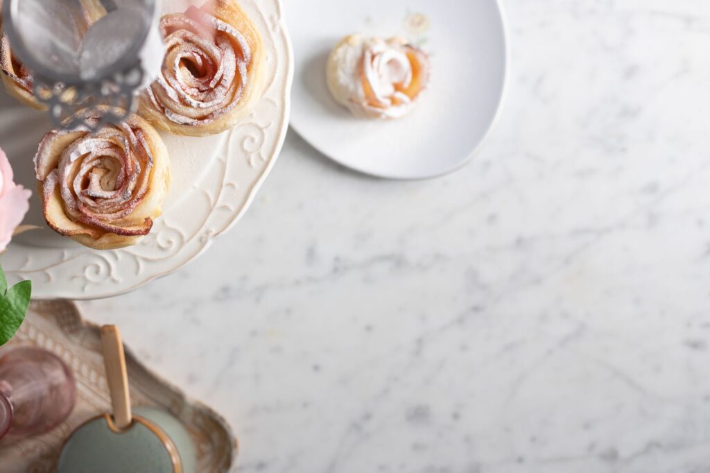 Élégantes pâtisseries en forme de rose à la pomme présentées sur une assiette décorative, parfaites pour des présentations de desserts raffinées.