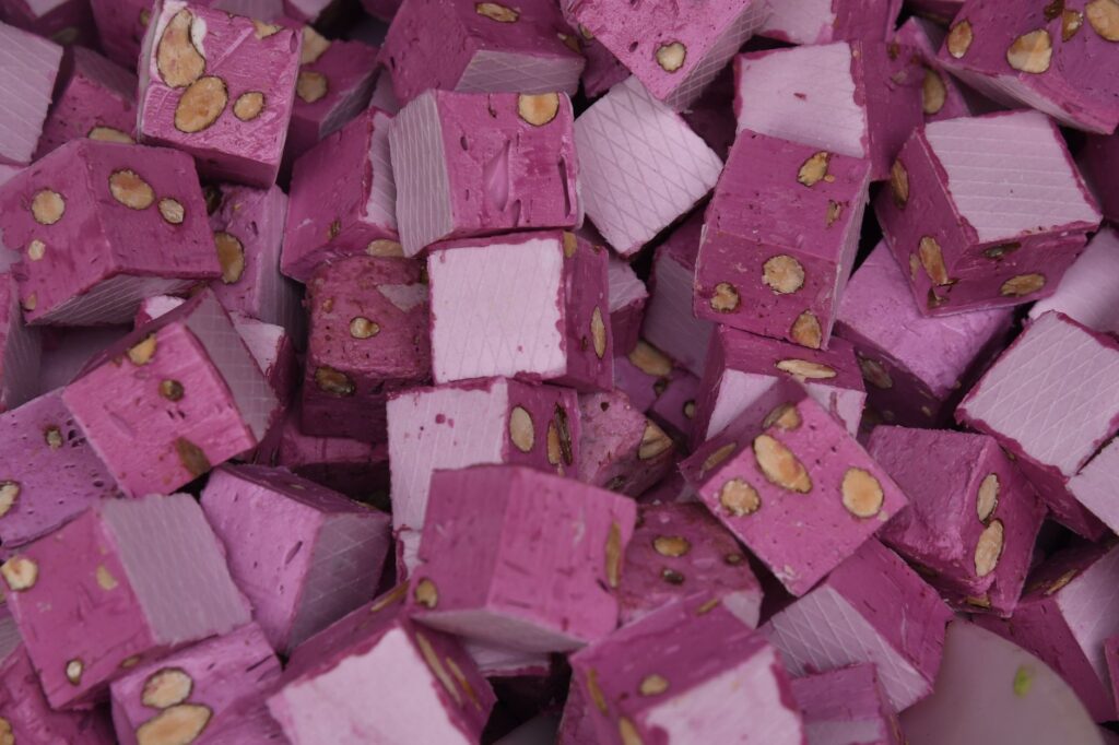 Un gros plan de cubes de nougat rose vibrants avec des noix, mettant en valeur la texture et la couleur.