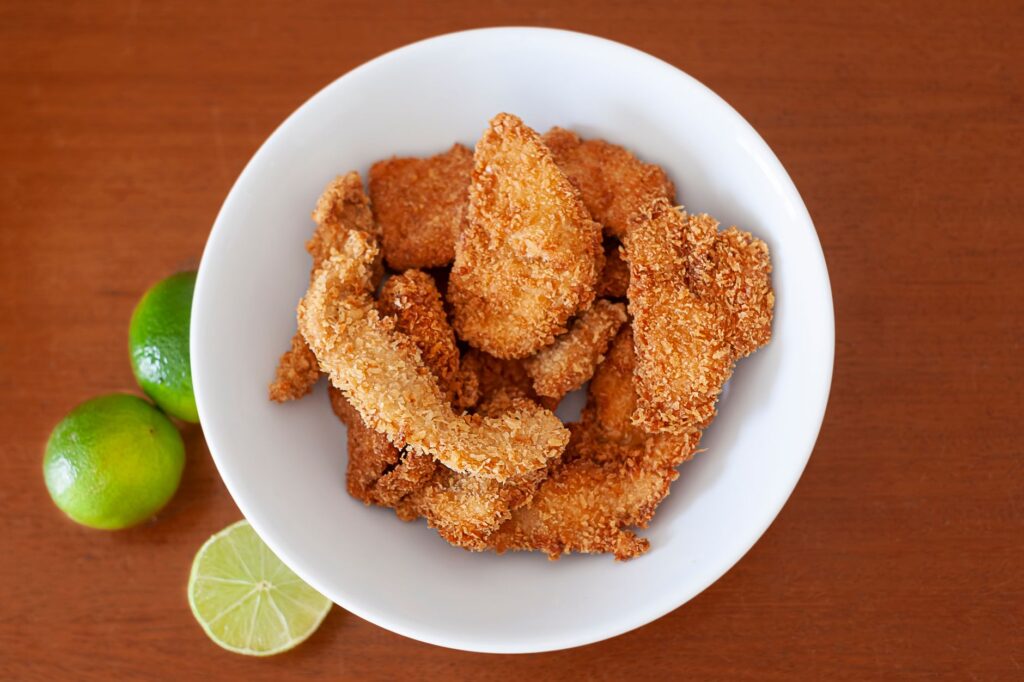 Des filets de poulet frits servis sur une assiette en céramique avec des citrons verts frais sur une table en bois.