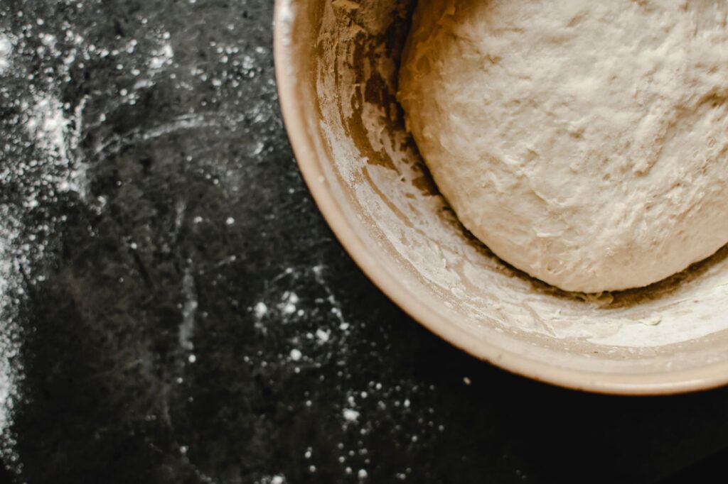 Vue aérienne de pâte dans un bol sur une surface farinée, prête à être cuite.