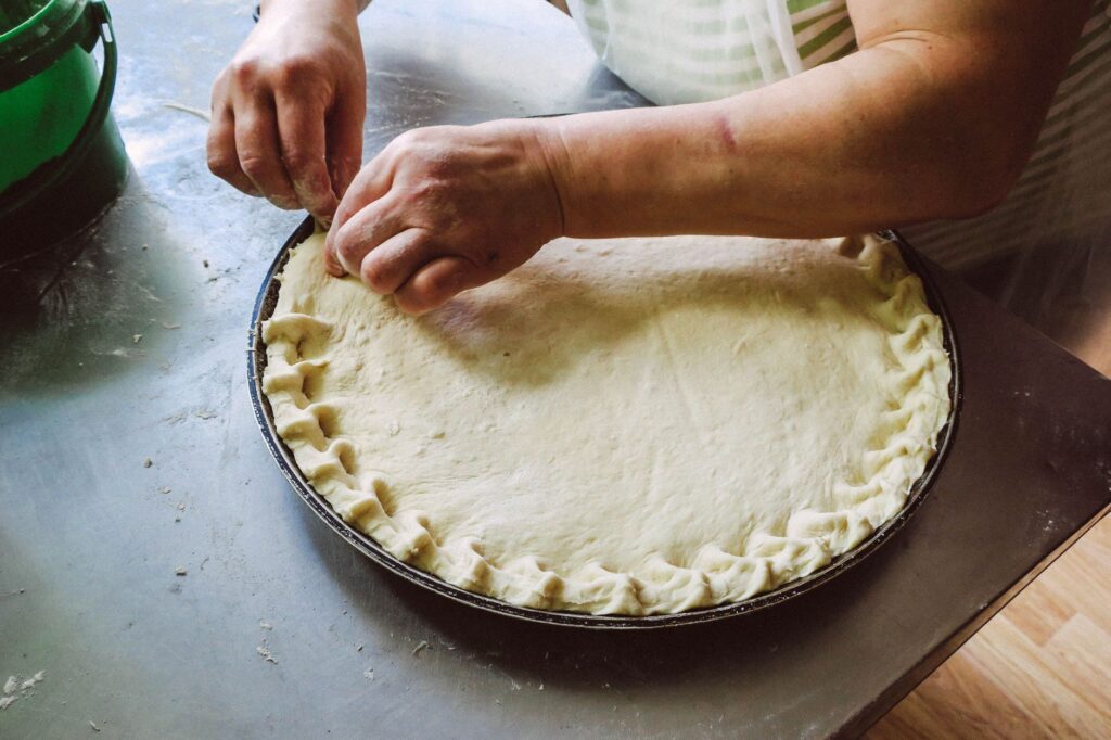 Mains façonnant une pâte à tarte sur un plateau de cuisson, mettant en valeur la préparation de nourriture faite maison.