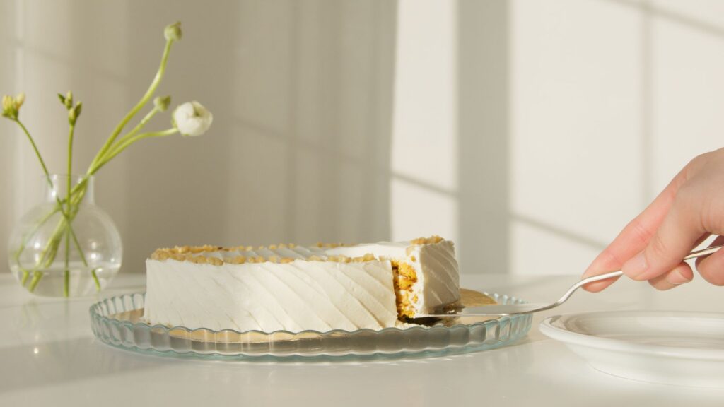 Une main prenant une part de gâteau élégamment glacé sur une table ensoleillée.