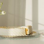 Une main prenant une part de gâteau élégamment glacé sur une table ensoleillée.