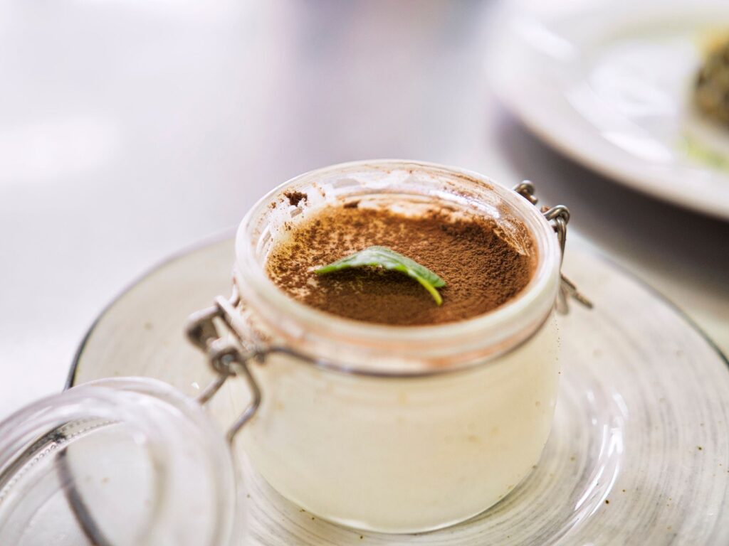 Gros plan sur un dessert crémeux de tiramisu en pot, garni de cacao et de feuille de menthe.