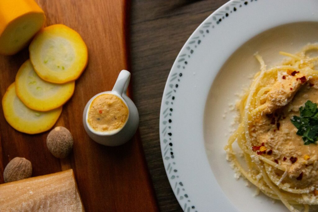 Délicieuses pâtes présentées avec une sauce crémeuse, des épices et des herbes fraîches, stylisées avec des ingrédients à côté.