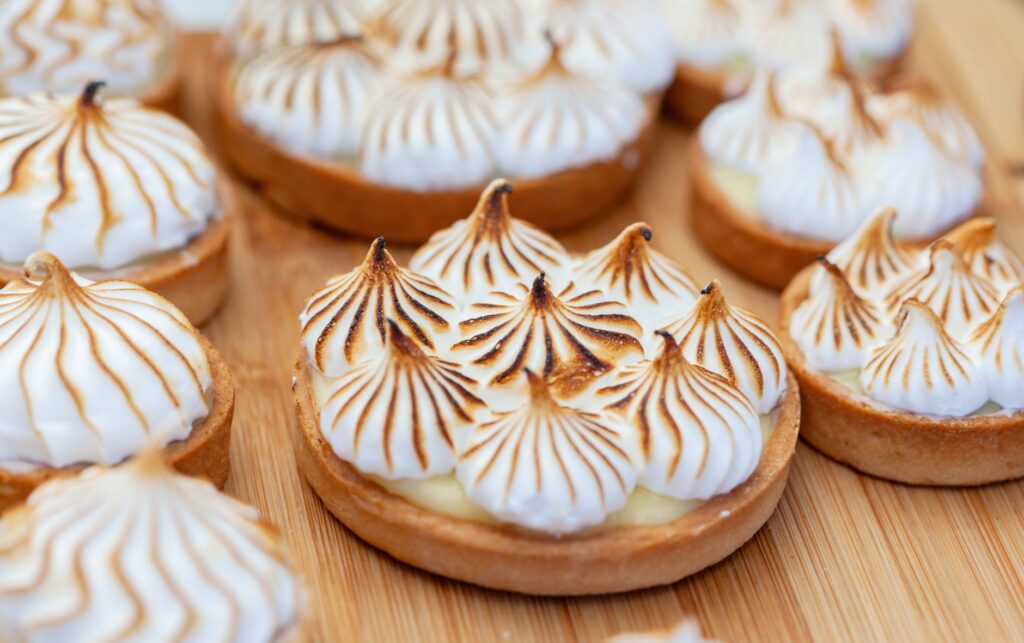 Gros plan de tartelettes au citron meringuée fraîchement cuites avec des sommets dorés sur une surface en bois.