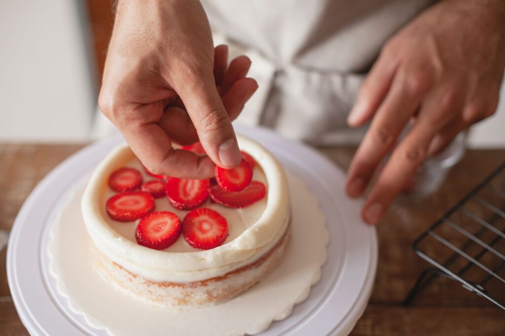 Gros plan sur les mains d'un chef plaçant artistiquement des tranches de fraise sur un gâteau.