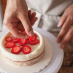 Gros plan sur les mains d'un chef plaçant artistiquement des tranches de fraise sur un gâteau.
