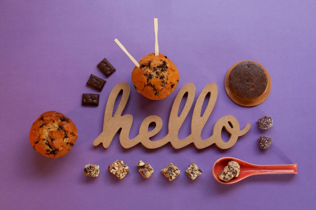 Une vue de dessus de chocolats variés et de muffins avec un panneau 'Bonjour' sur une surface violette.