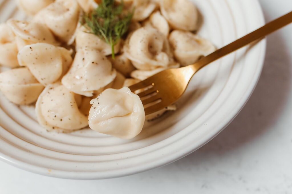 Délicieuse prise de vue rapprochée de raviolis frais avec des herbes sur une assiette blanche et une fourchette.