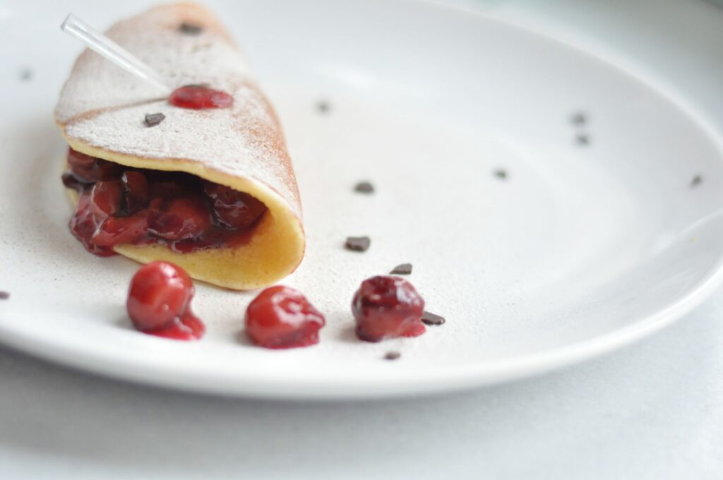 Délicieuse crêpe remplie de compote de cerises, saupoudrée de sucre glace sur une assiette blanche.