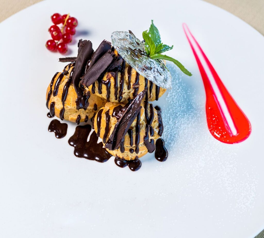 Somptueux profiteroles garnis de sauce au chocolat et de baies, présentés sur une assiette blanche.
