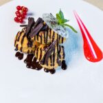 Somptueux profiteroles garnis de sauce au chocolat et de baies, présentés sur une assiette blanche.