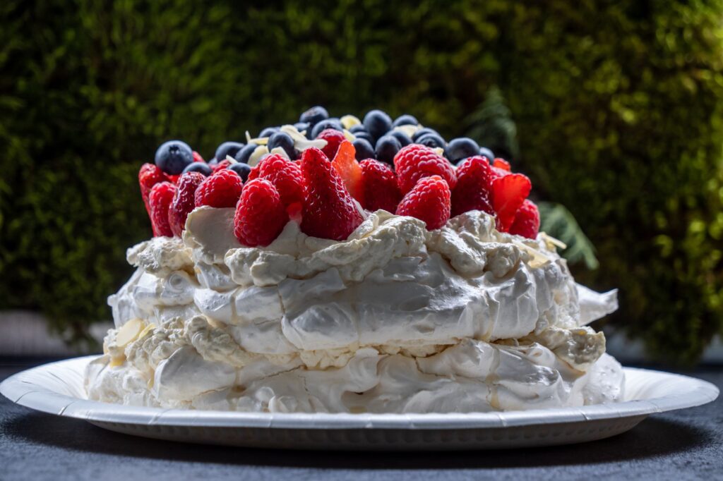 Gâteau Pavlova à couper le souffle surmonté de fraises fraîches, de framboises et de myrtilles sur une assiette.