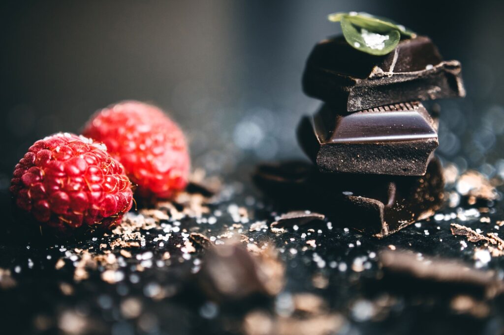 Gros plan artistique de morceaux de chocolat noir avec des framboises fraîches, parfait pour des visuels de dessert.