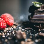 Gros plan artistique de morceaux de chocolat noir avec des framboises fraîches, parfait pour des visuels de dessert.