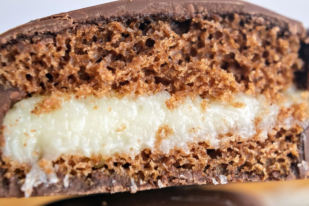 Photo macro d'un gâteau enrobé de chocolat avec une garniture crémeuse, mettant en valeur la texture et les couches.