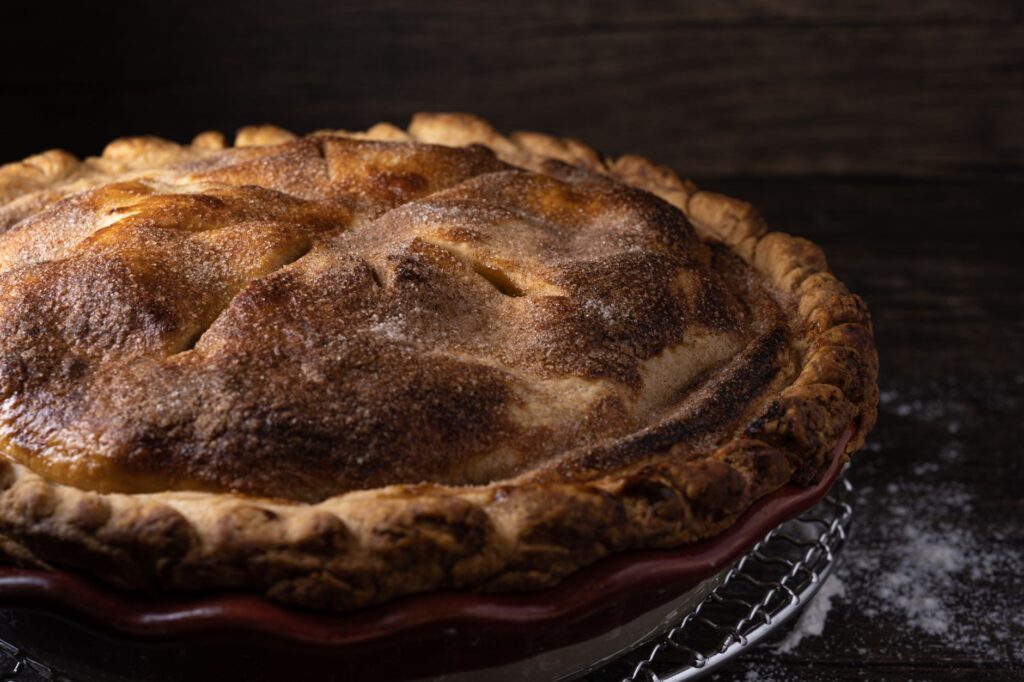 Une délicieuse tarte aux pommes faite maison avec une croûte dorée sur une grille évoque une ambiance rustique et chaleureuse.