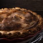 Une délicieuse tarte aux pommes faite maison avec une croûte dorée sur une grille évoque une ambiance rustique et chaleureuse.